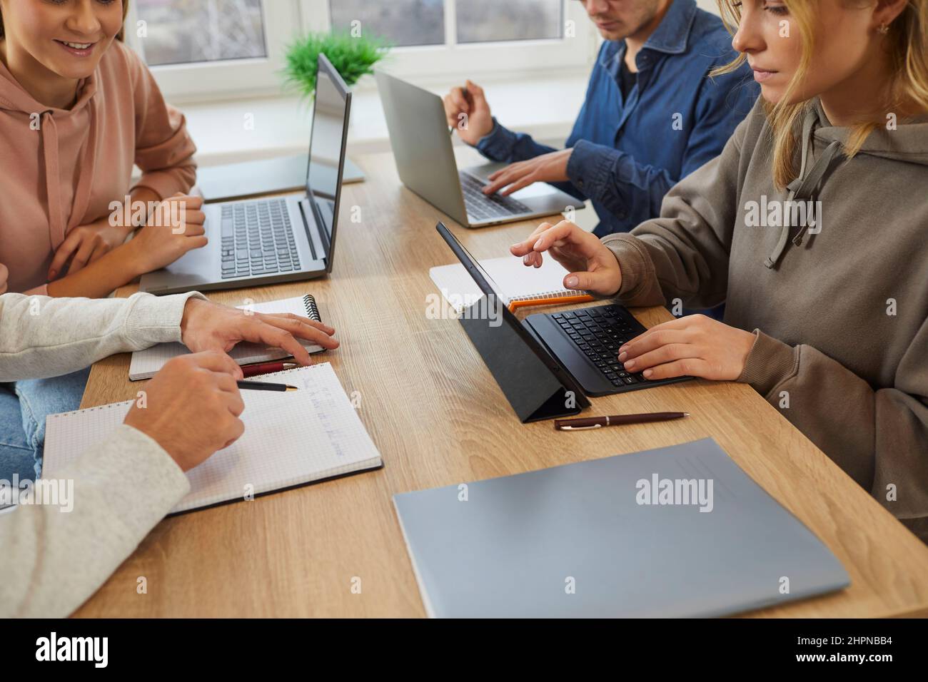 Group of university students sitting at desk, using laptops and tablets and sharing study notes Stock Photo