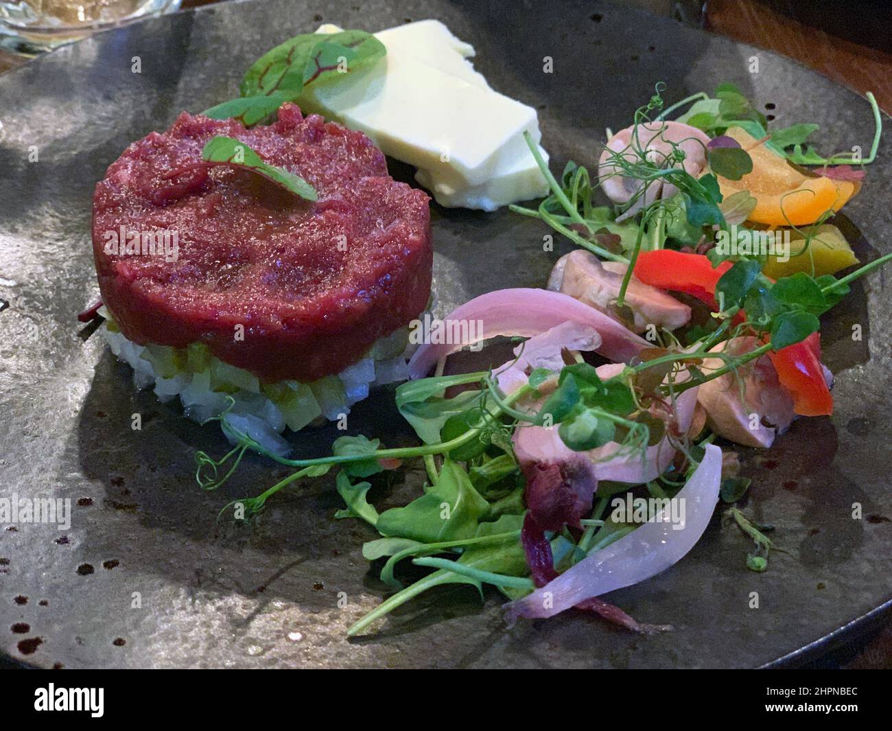 The raw meat tartare with greens and rice on a black dish composition Stock Photo