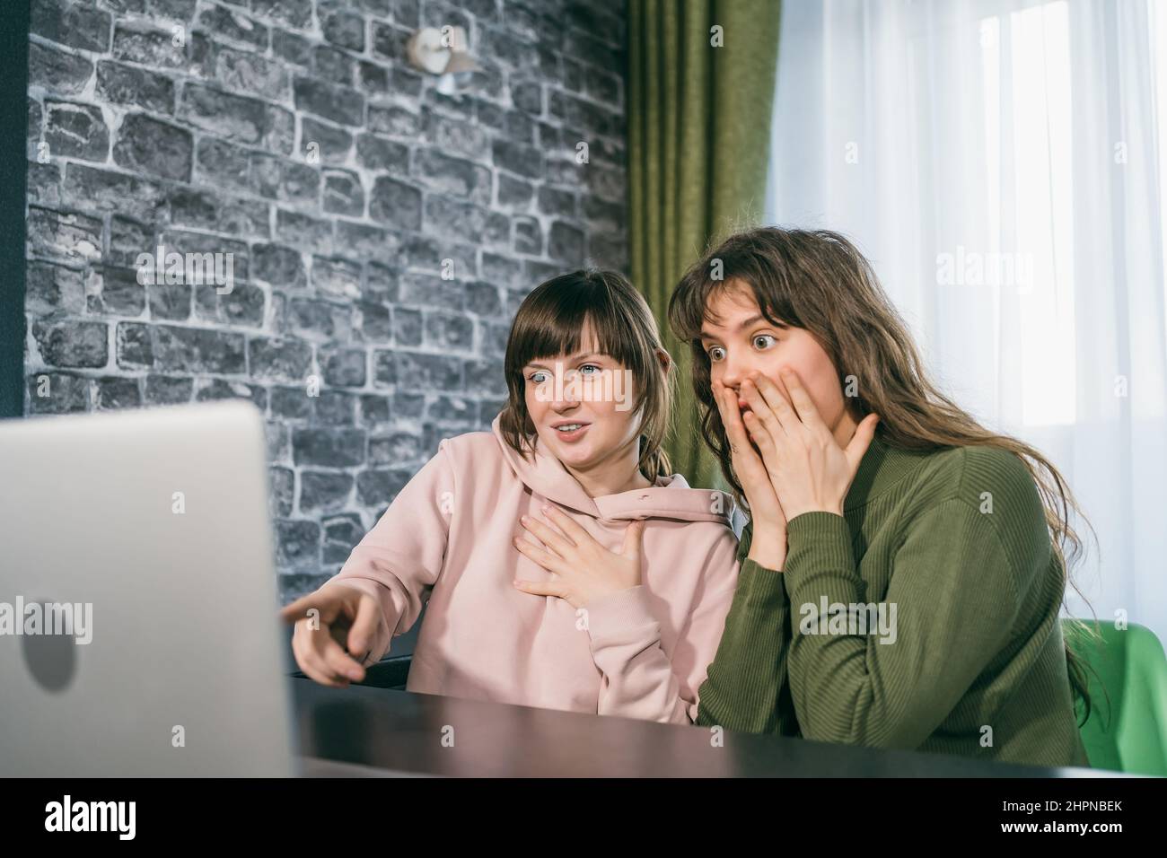 Two young women receive good news by internet or winning lottery looking at laptop. Happy surprised girl gets positive emotion. Stock Photo