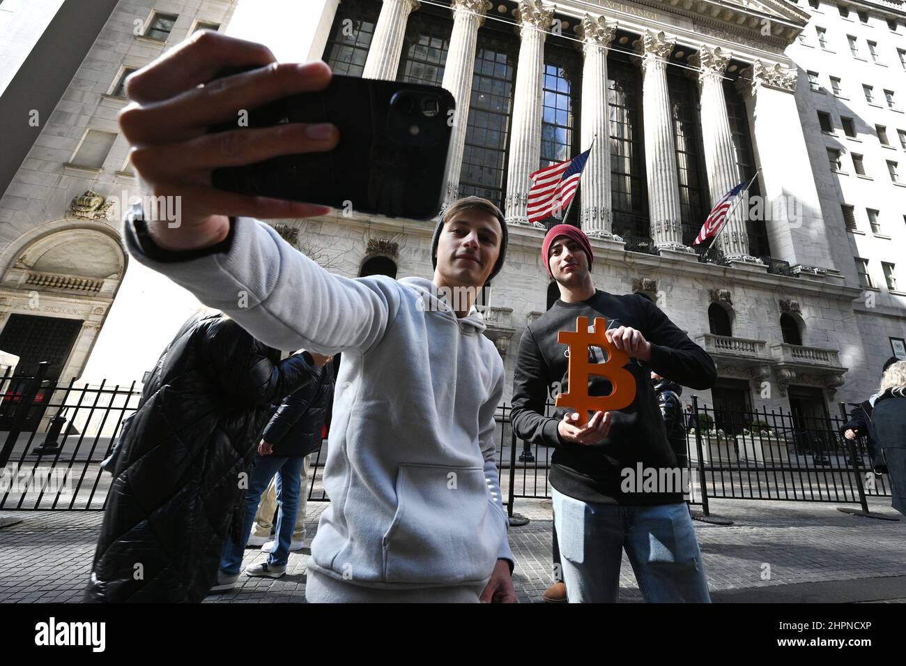 New York, USA. 22nd Feb, 2022. Friends photograph themselves with the Bitcoin currency emblem (by artist Leonid Sukala) in front of the New York Stock Exchange as the DOW reacts to the news that Russian President Vladimir Putin ordered troops into Ukraine, New York, NY, February 22, 2022. Stocks tumbled as crude oil price surged while the United States and its allies announced economic sanctions against Russia for its incursion into Ukraine. (Photo by Anthony Behar/Sipa USA) Credit: Sipa USA/Alamy Live News Stock Photo
