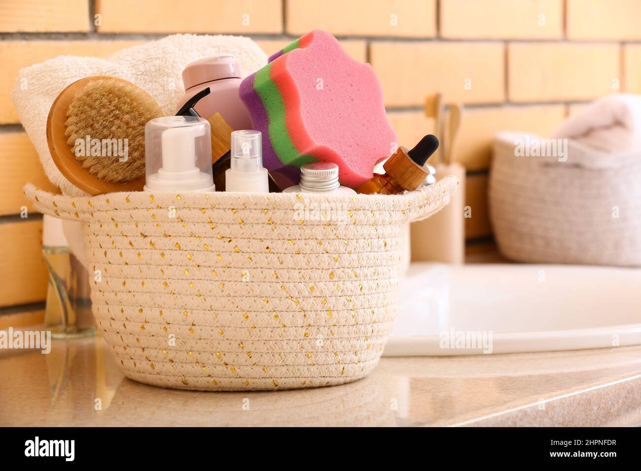 Basket with different cosmetic products and bath accessories on table