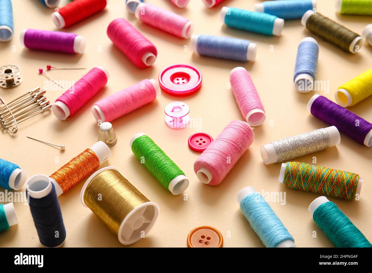 Thread spools with buttons and pins on beige background Stock Photo