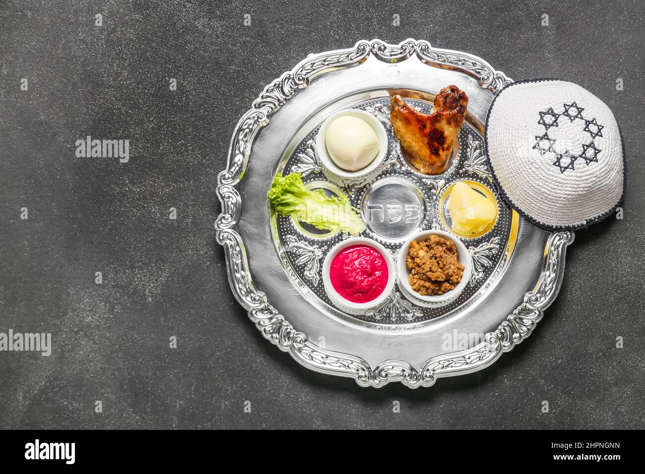 Passover Seder plate with traditional food and kippah on dark ...