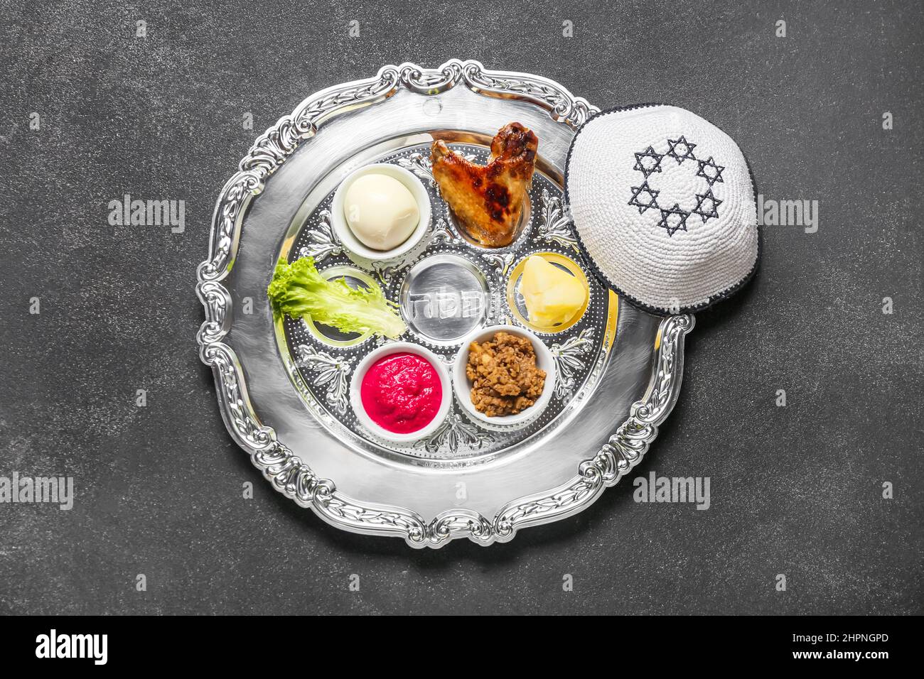 Passover Seder plate with traditional food and kippah on dark ...