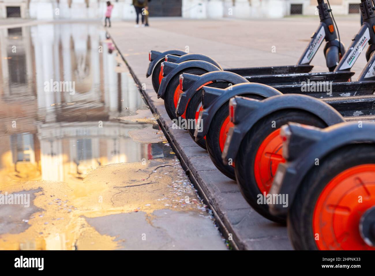 A row of sharing electric scooters wheels in a public city square in Modena, Italy Stock Photo