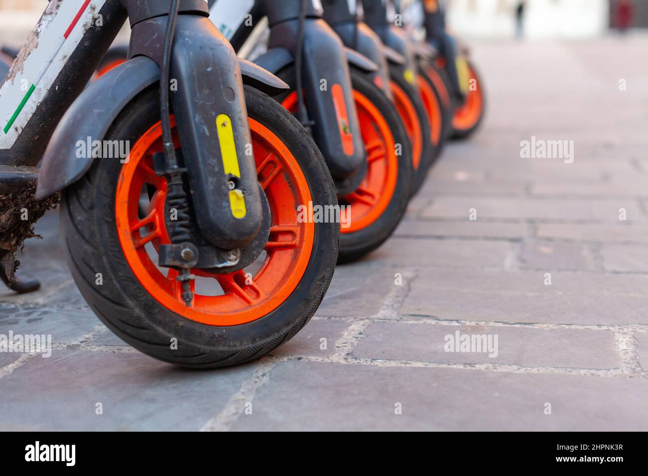 A row of sharing electric scooters wheels in a public city square in Modena, Italy Stock Photo