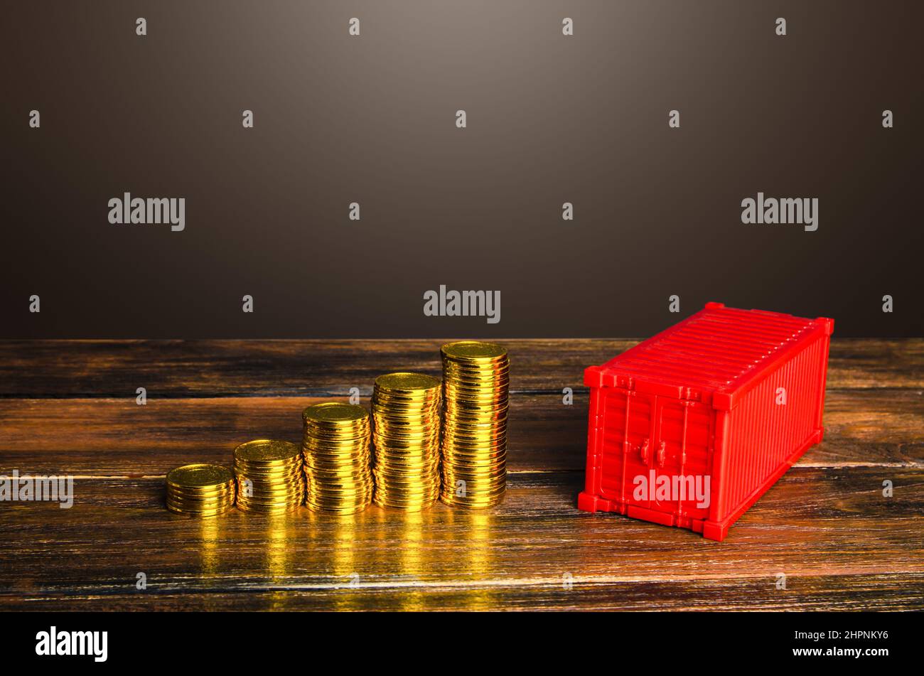 Increasing stacks of coins and a cargo shipping container. High container rental prices, global transportation shortages and trade imbalances. Tariffs Stock Photo