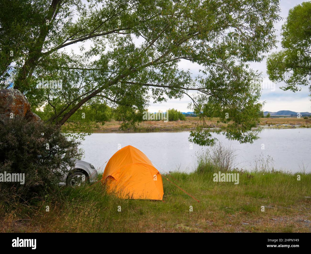 Freedom camping with a tent on the edge of a lake in New Zealand, in the summer is a popular activity for travellers and fishermen Stock Photo