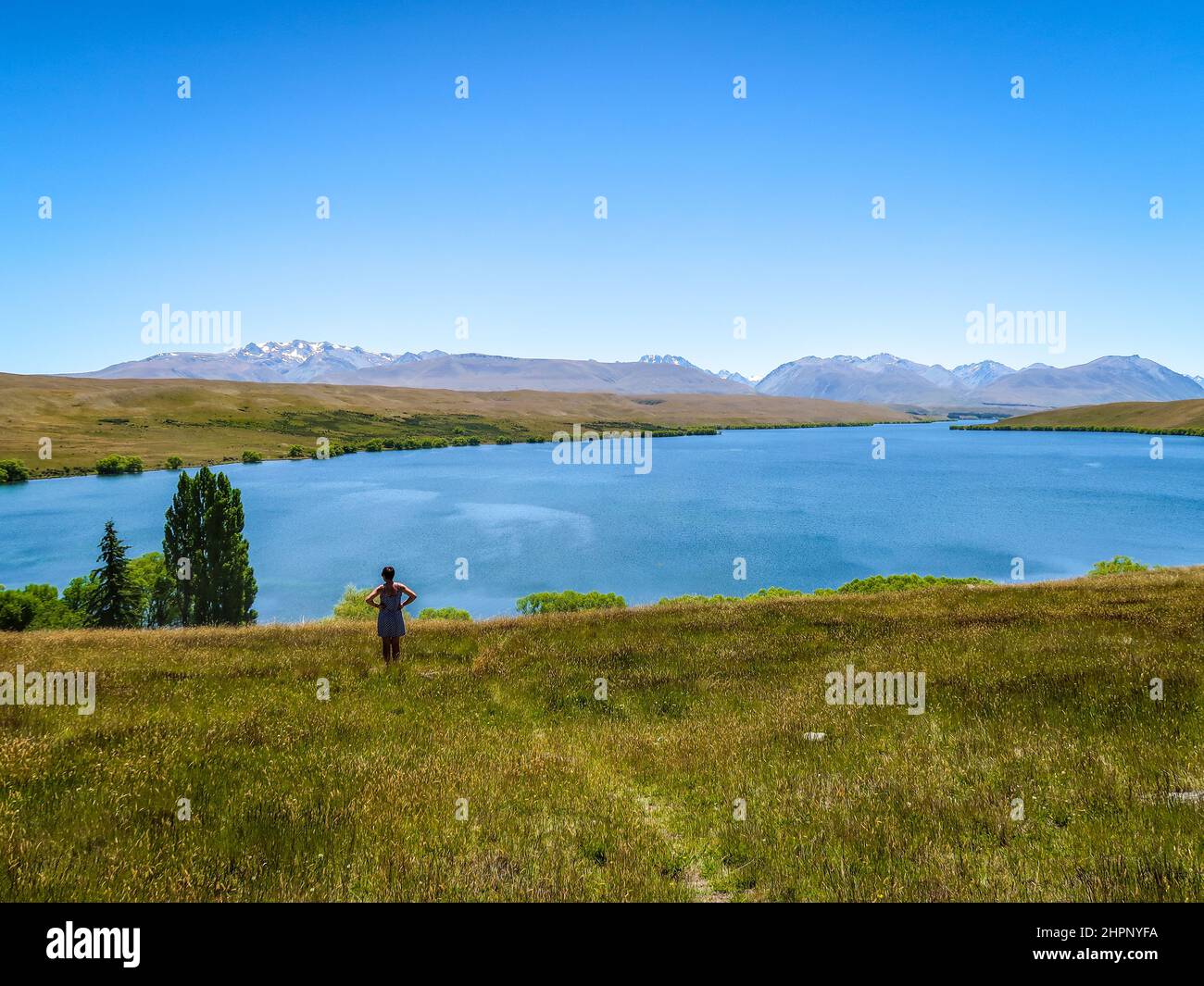 A female tourists stops to enjoy the scenic view towards the mountains above Lake Alexandrina, in Canterbury, New Zealand Stock Photo