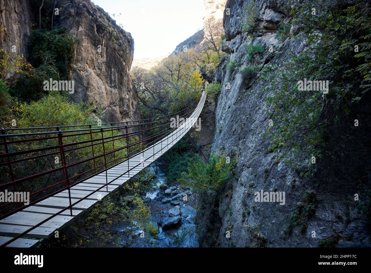 Wooden hanging bridge in between rocky cliffs over the river Stock