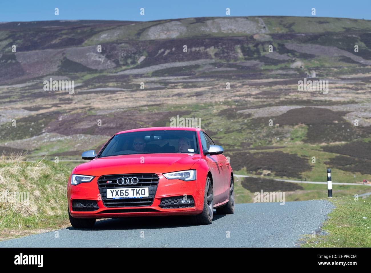 Red Audi car driving along a single track road over moorland in the Yorkshire Dales National Park, UK. Stock Photo