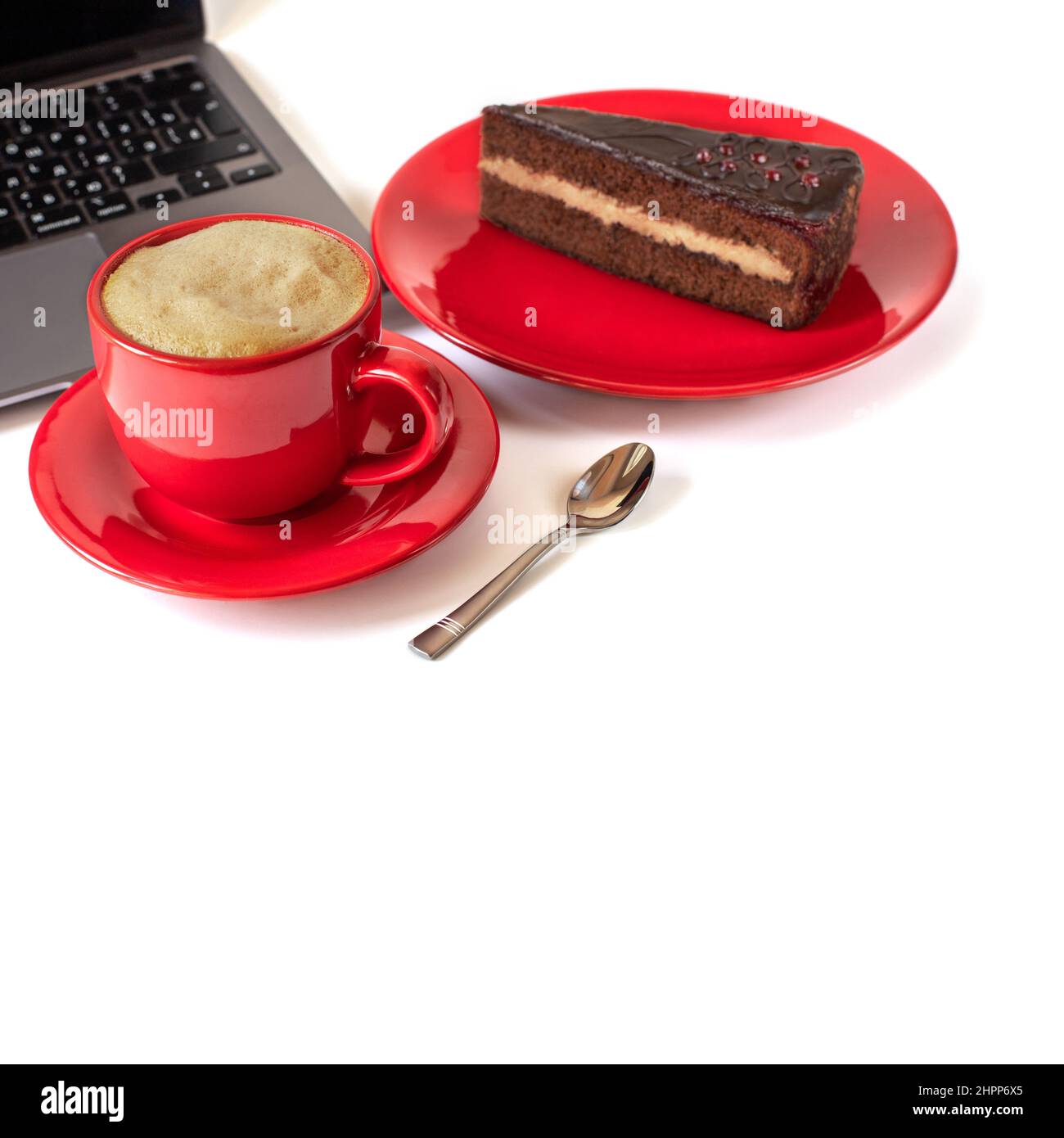 On the table is a cup of coffee with foam, a cake on a saucer and a laptop. Selective focus. Isolate Stock Photo