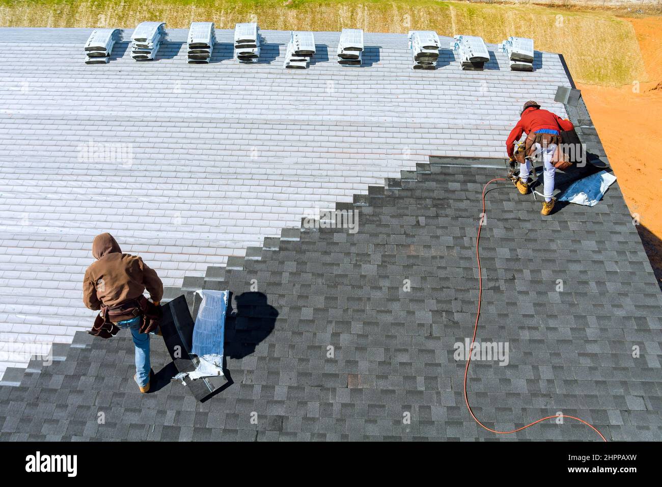 Worker hands installing bitumen roof shingles with air hammer and nail