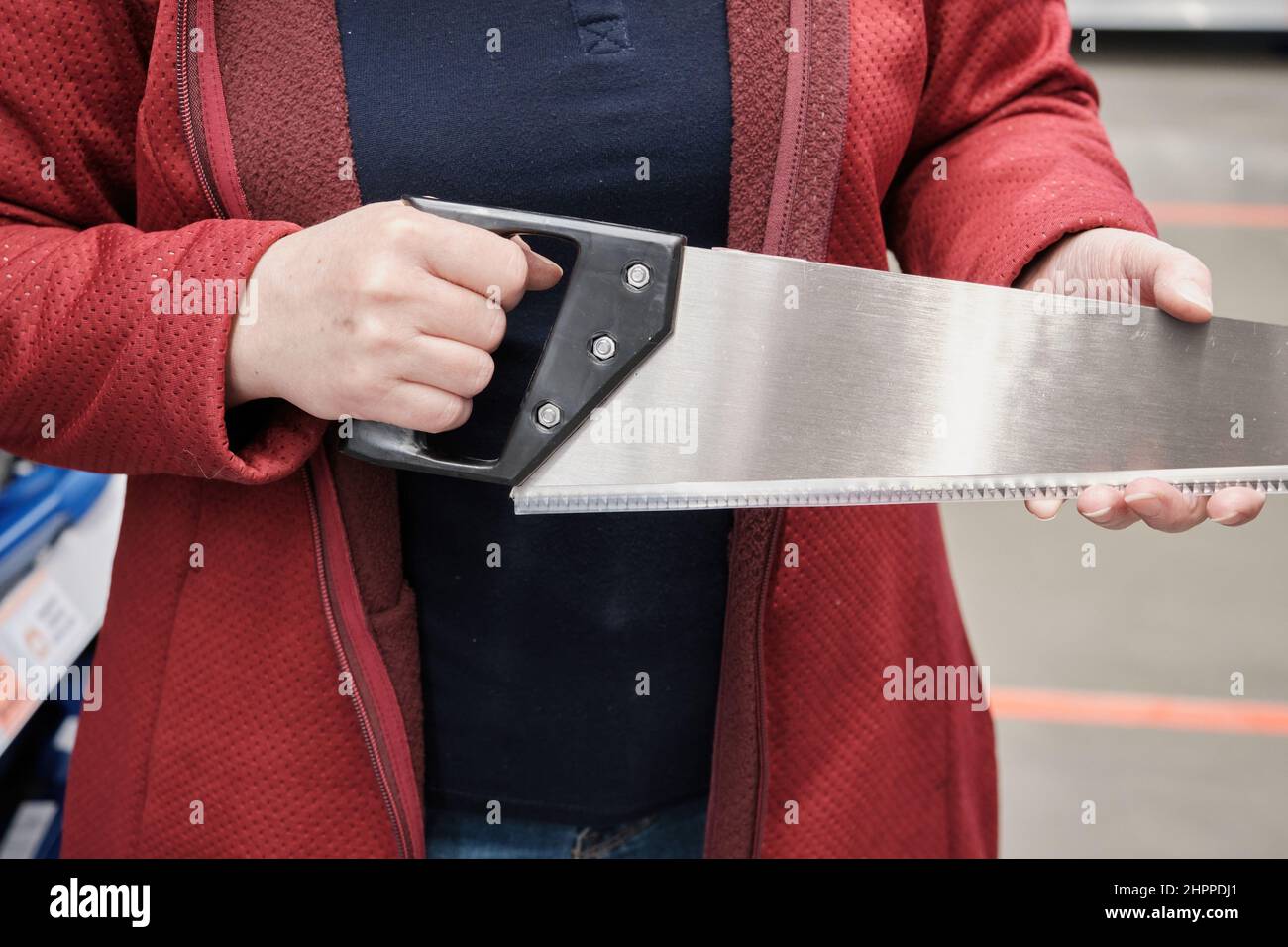 Girl in building store chooses hand saw. She removes protection from iron teeth Stock Photo