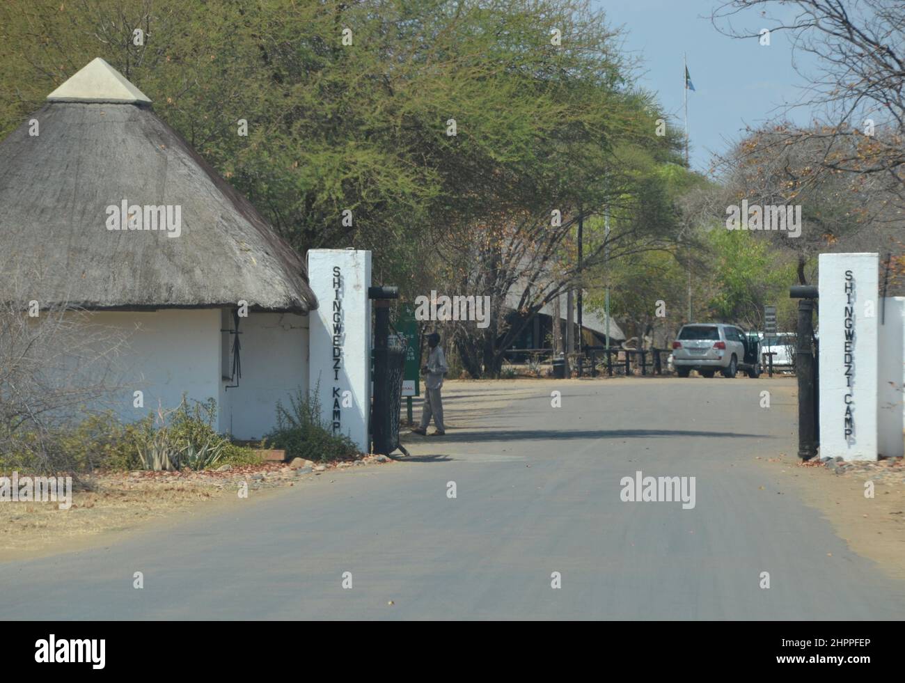 Retro security gate entrance to Shingwidzi Rest Camp in Kruger National Park with a thatched rondawel or cottage gatehouse and whitewashed walls Stock Photo