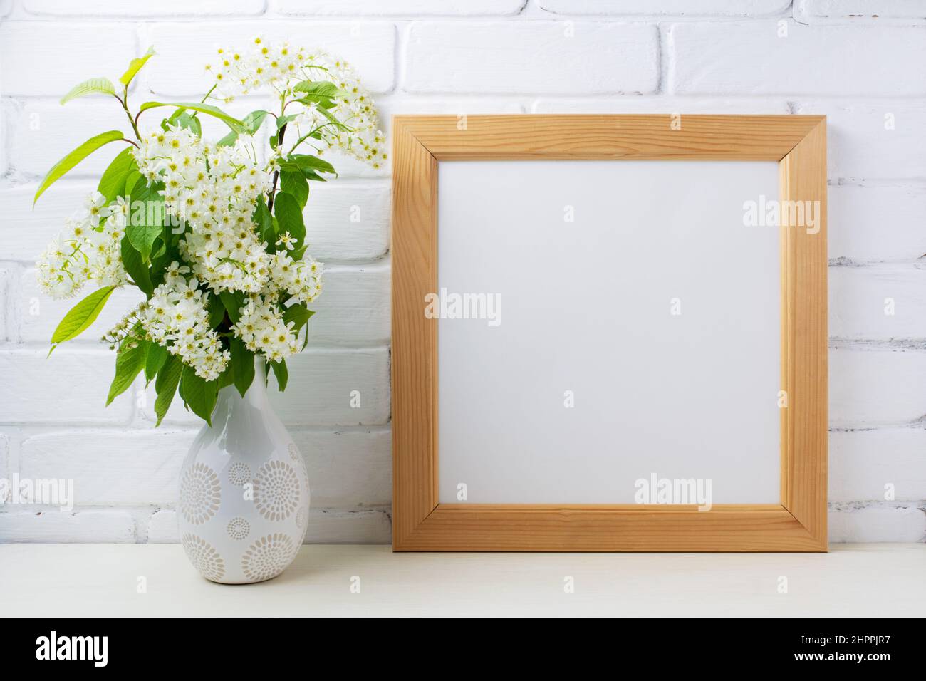 Wooden square picture frame mockup with blooming bird cherry branch in the vase. Empty frame mock up for presentation design. Template framing for mod Stock Photo