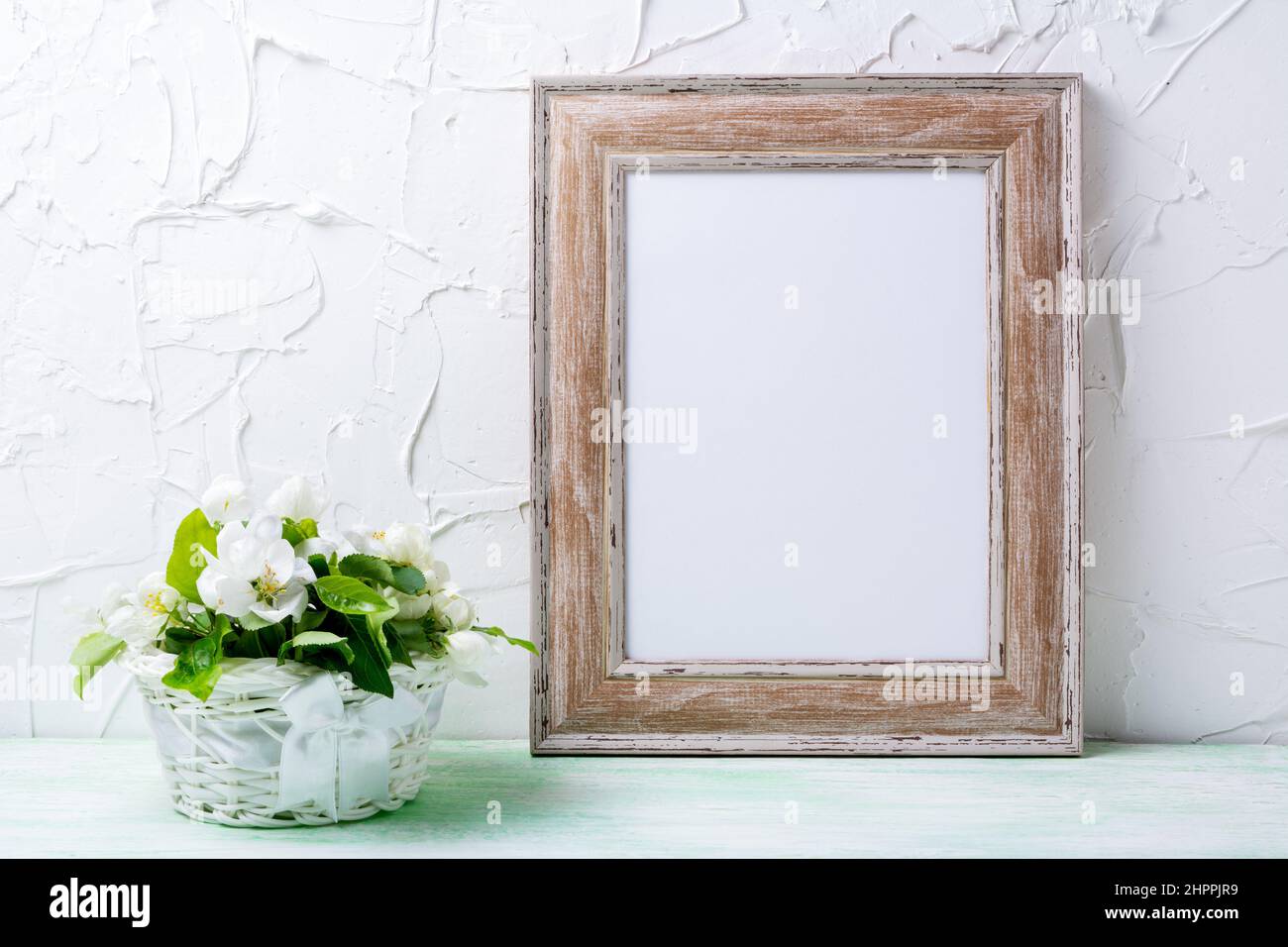 Wooden picture frame mockup with apple blossom in the white wicker basket. Empty frame mock up for presentation design. Template framing for modern ar Stock Photo