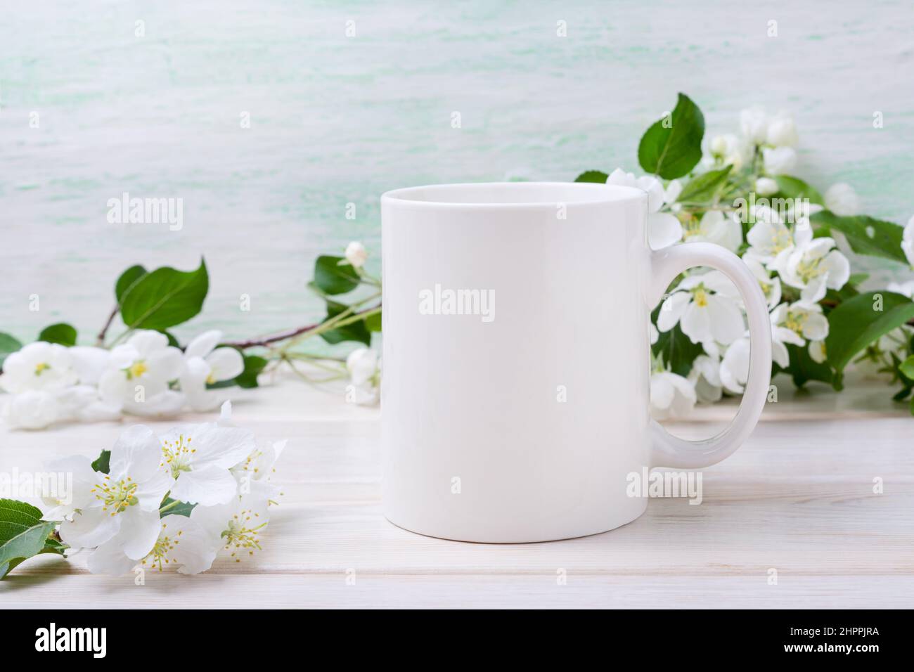 White coffee mug mockup with tender apple blossom flowers. Empty mug mock up for design promotion, styled template Stock Photo