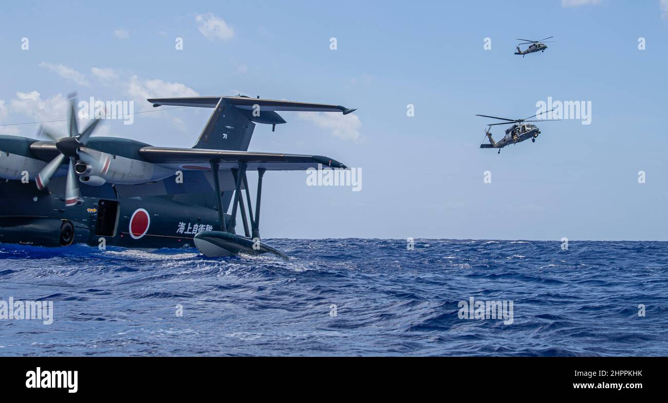 A Japanese ShinMaywa US-2 with the 71st Air Rescue Squadron floats in the ocean while U.S. Air Force HH-60G Pave Hawks with the 33rd Rescue Squadron hover nearby during exercise Cope North 22 at the Island of Tinian near Andersen Air Force Base, Guam, Feb. 14, 2022. Japanese and U.S. Air Force members trained together in participation of Cope North 2022, multilateral U.S. Pacific Air Forces-sponsored field training exercise conducted annually at Andersen AFB, Guam focused on combat air forces’ large-force employment and humanitarian assistance and disaster relief training to enhance interopera Stock Photo