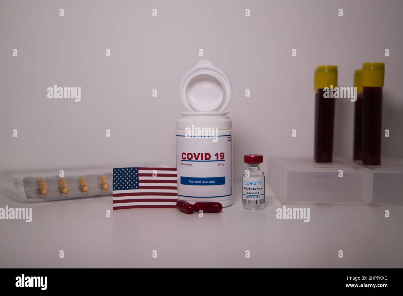 Covid19 pill bottle with several pills outside the bottle and a US flag on a lab bench Stock Photo