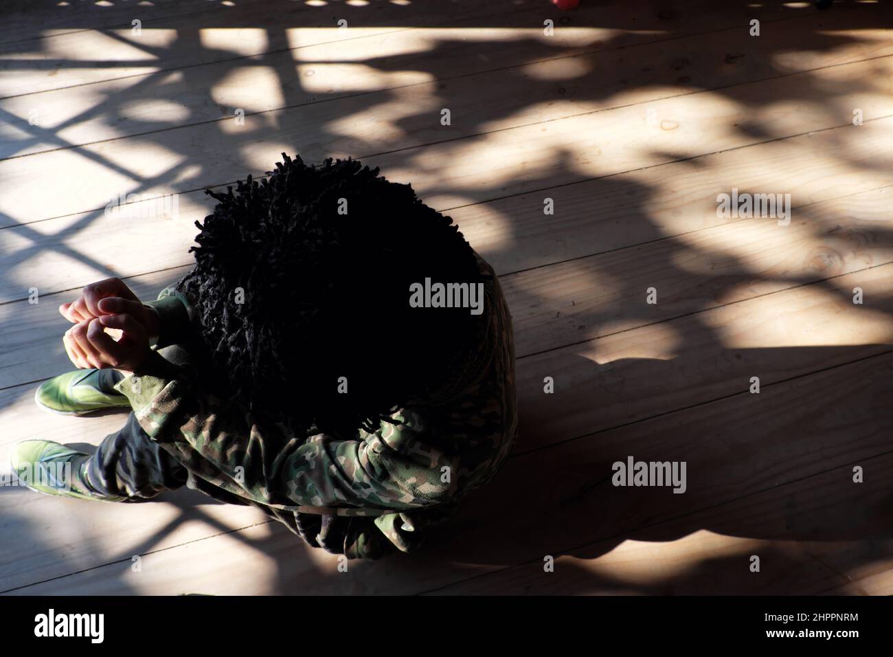 Top view alone Vietnamese woman sit indoor on wooden floor with drop shadow from door by sunny afternoon, people wear soldier clothes and ruffled hair Stock Photo