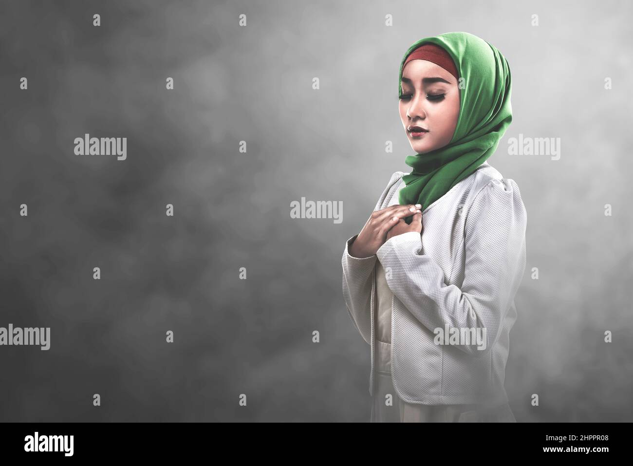 Asian Muslim woman in a veil standing while raised hands and praying ...