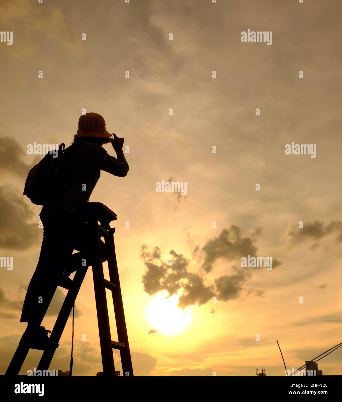 Amazing scene from Vietnamese woman when stay at home by social distancing, she make fun at sunset on rooftop by stand on ladder when sun go down to m Stock Photo