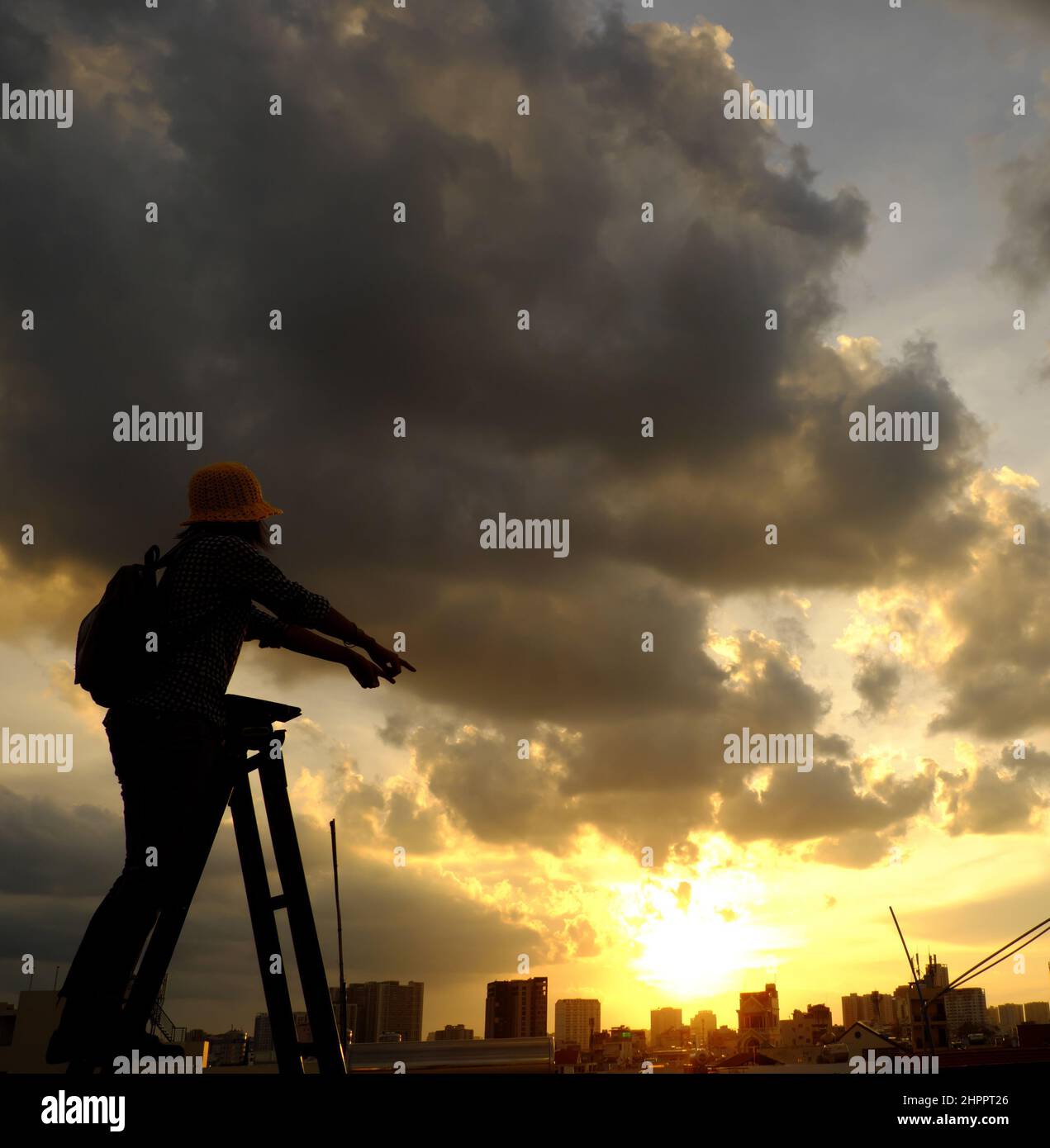 Amazing scene from Vietnamese woman when stay at home by social distancing, she make fun at sunset on rooftop by stand on ladder when sun go down to m Stock Photo