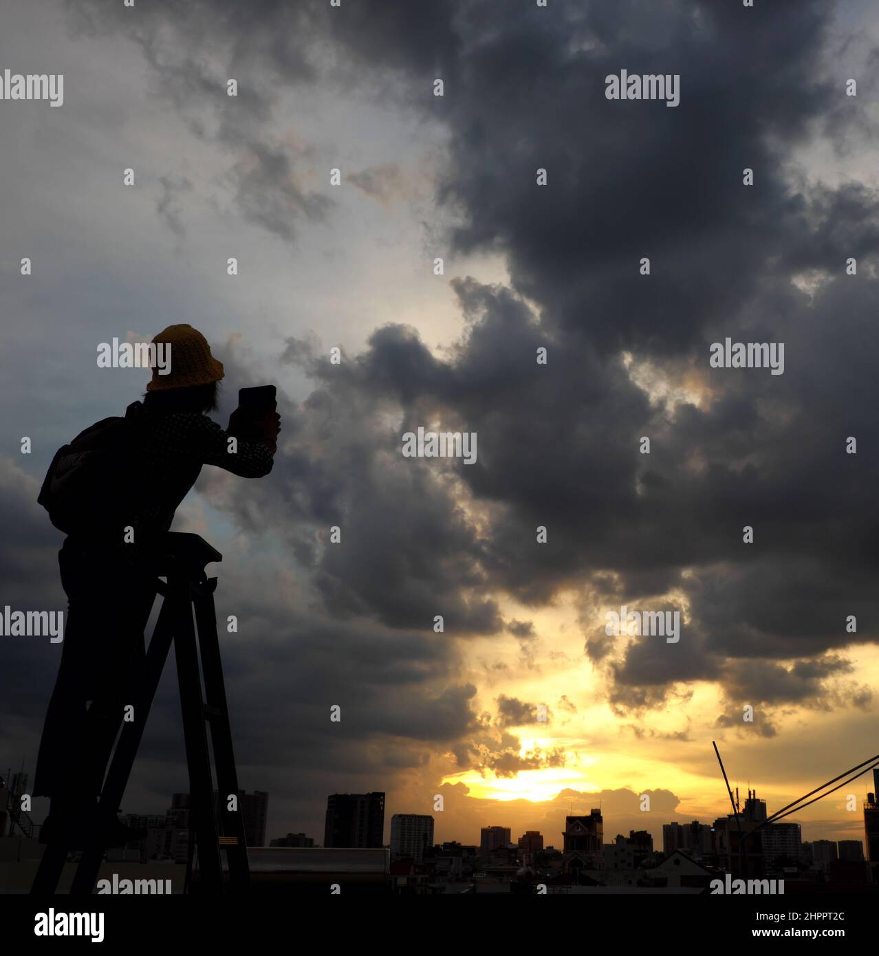 Amazing scene from Vietnamese woman when stay at home by social distancing, she make fun at sunset on rooftop by stand on ladder when sun go down to m Stock Photo