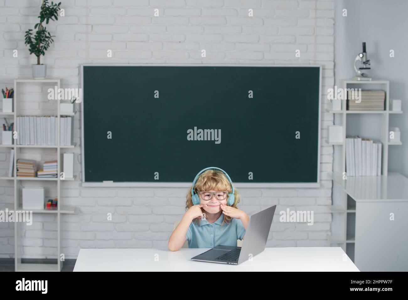 Cute boy wearing headphones, study with laptop in classroom, listening ...