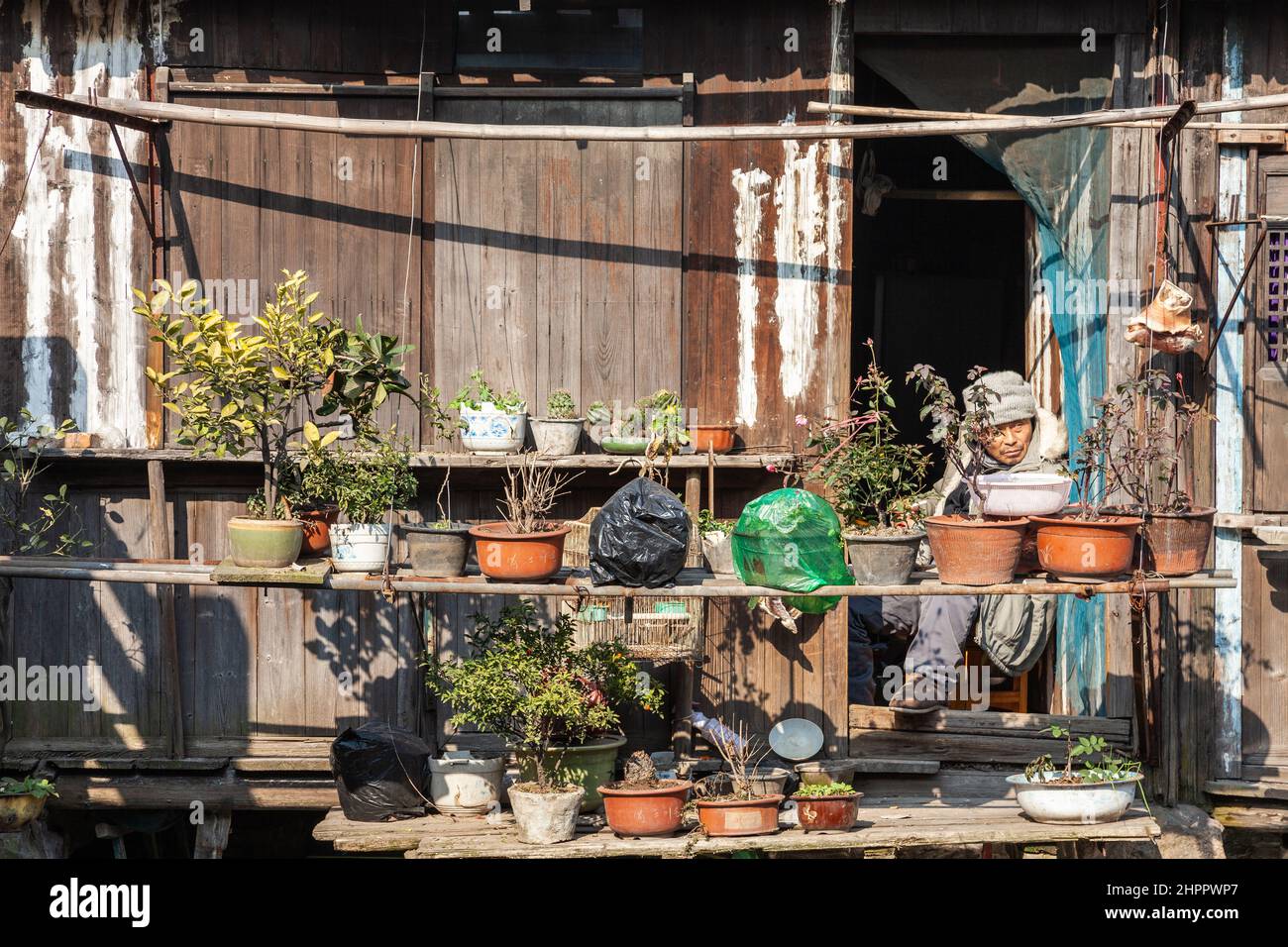 Man sitting on a balcony cluttered with various objects, trying to warm himself in the winter sun in the water village of Wenzhou, China Stock Photo