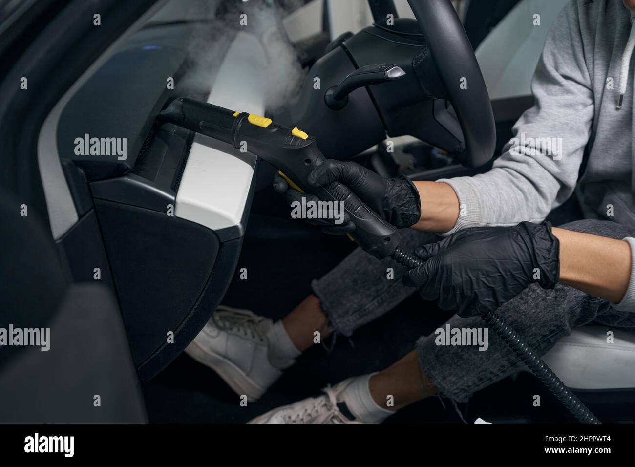 Experienced auto detailer steamcleaning car interior surfaces Stock