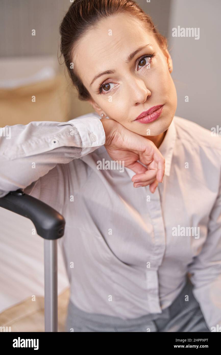 Low-spirited thoughtful woman with baggage sitting alone in hotel room Stock Photo