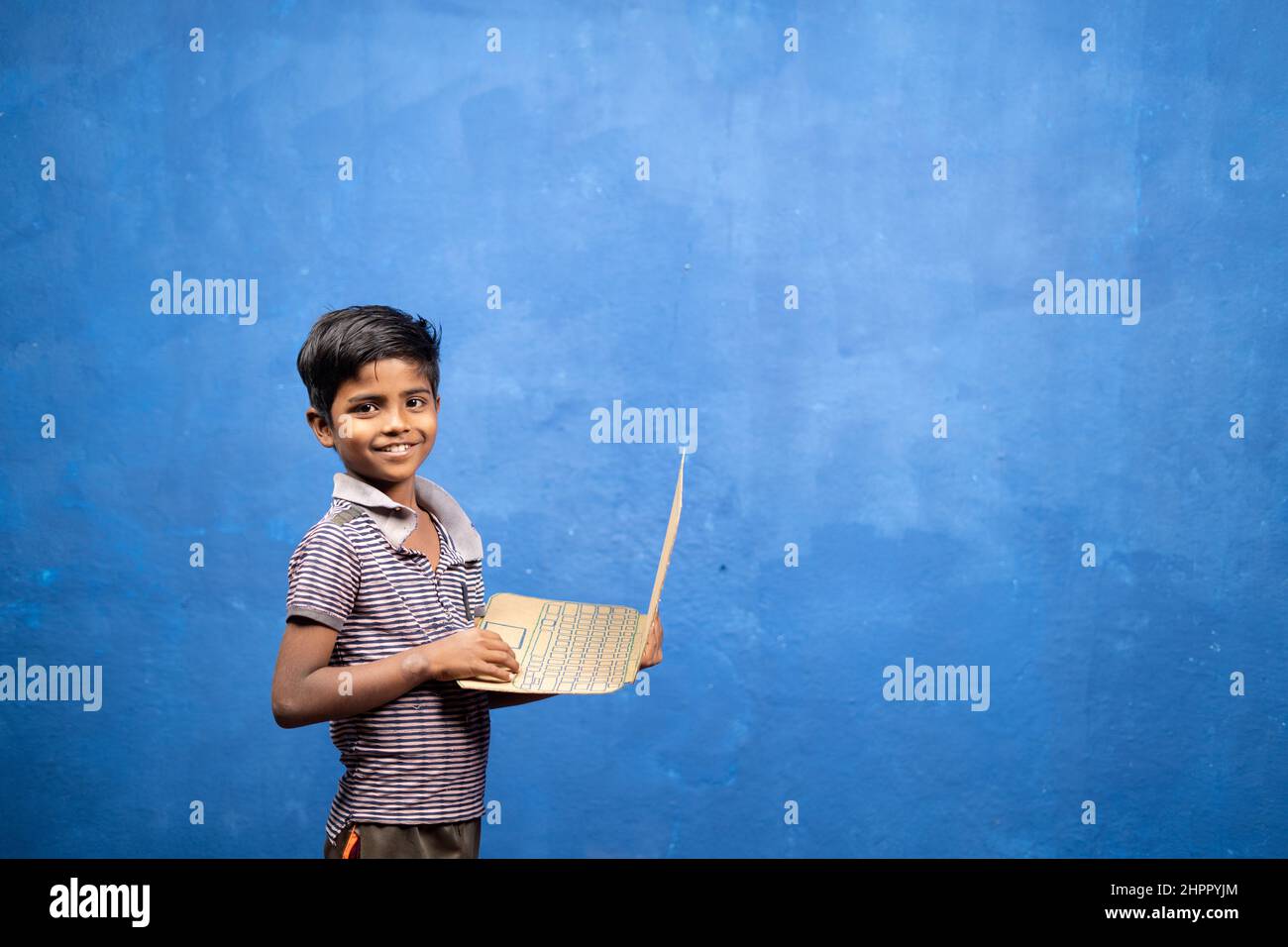 Smiling boy kid playing with cardboard laptop by looking at camera - concept of entertainment, childwood playful lifestyle and poverty Stock Photo