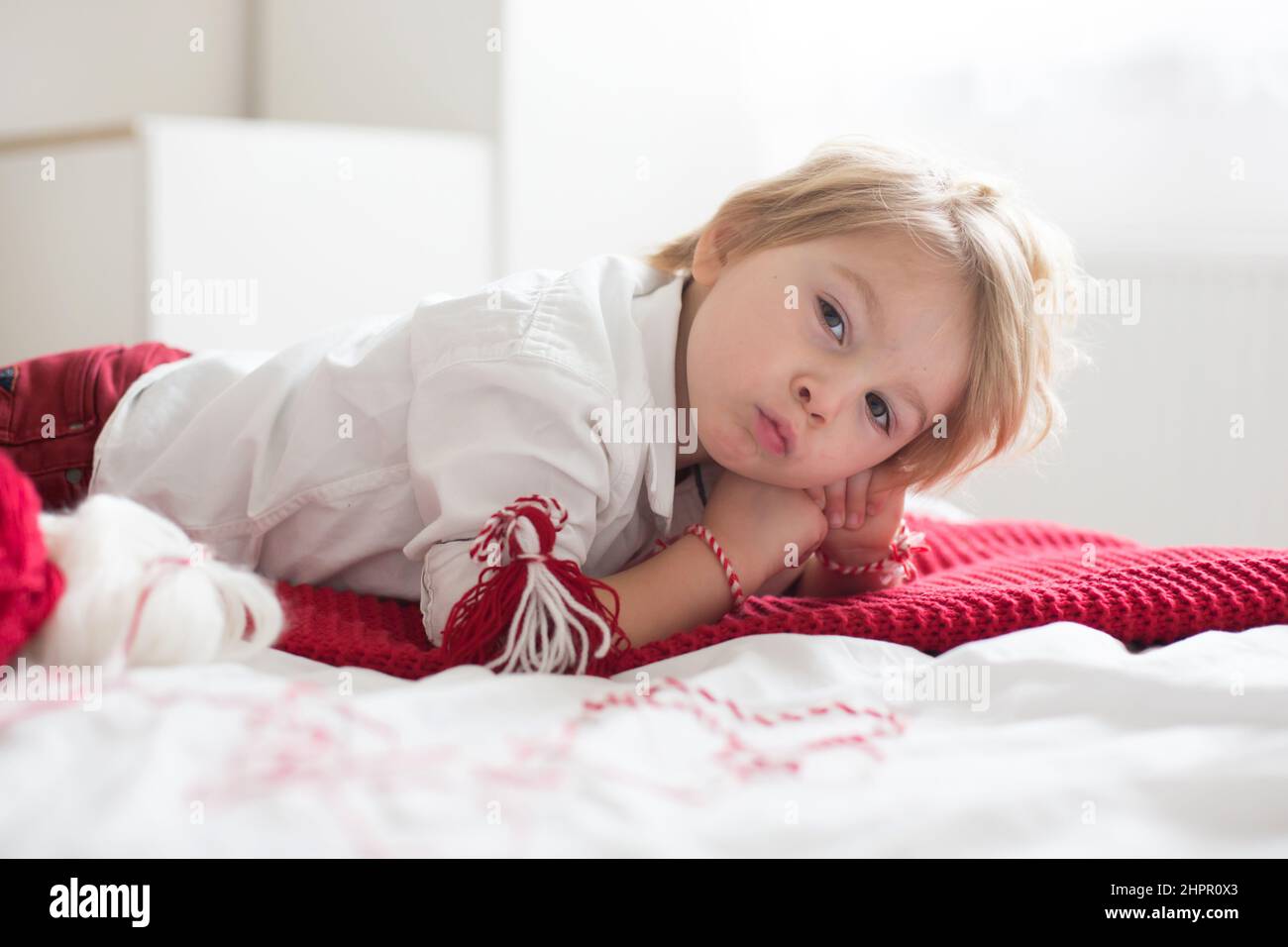 Cute child, blond boy, playing with white and red bracelet, called