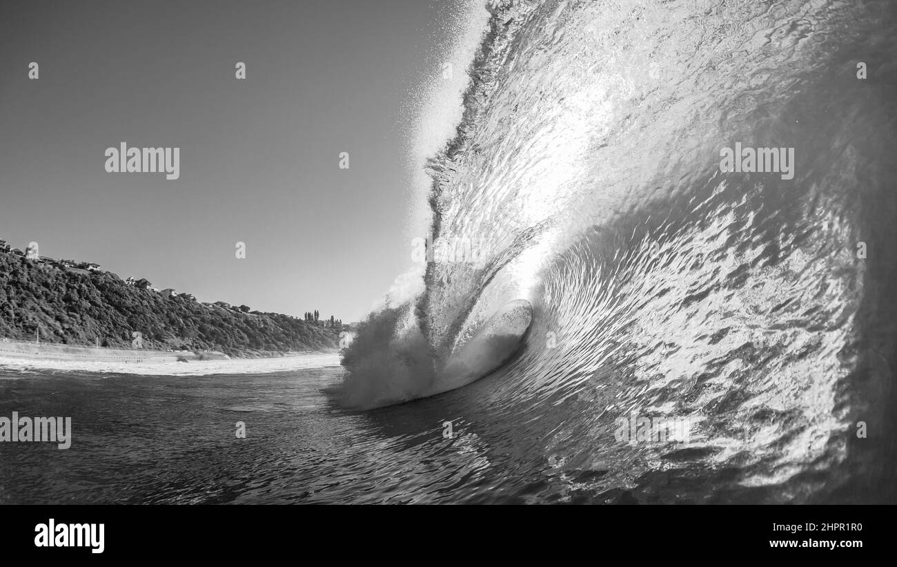 Ocean wave hollow crashing sea water onto shallow reef with back-light sun close-up swimming in natures power in black and white photo. Stock Photo