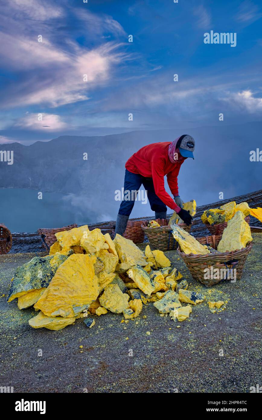 The view of sulfur miners who climb and go down to the crater is also amazing. A man puts about 10 kg of yellowish stone in to his basket, before he d Stock Photo