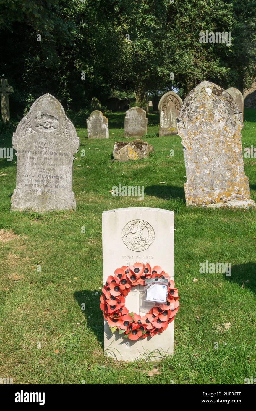 A war grave with a poppy wreath in a small country churchyard at West Winch, Norfolk. Stock Photo