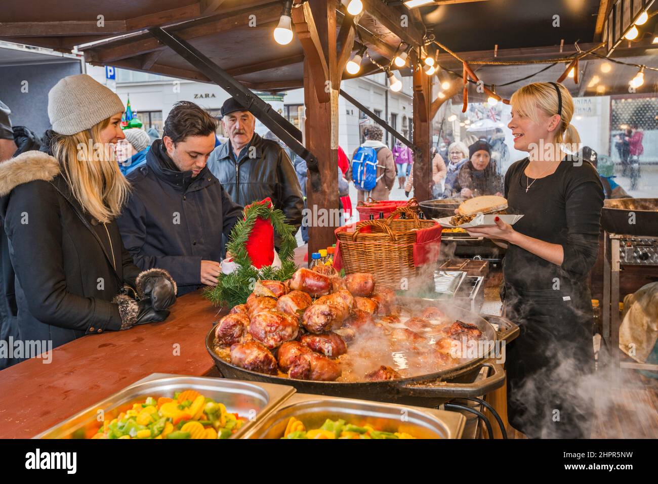 Customers, hot food at street stand at Christmas market, Main Market Square, Kraków, Poland Stock Photo