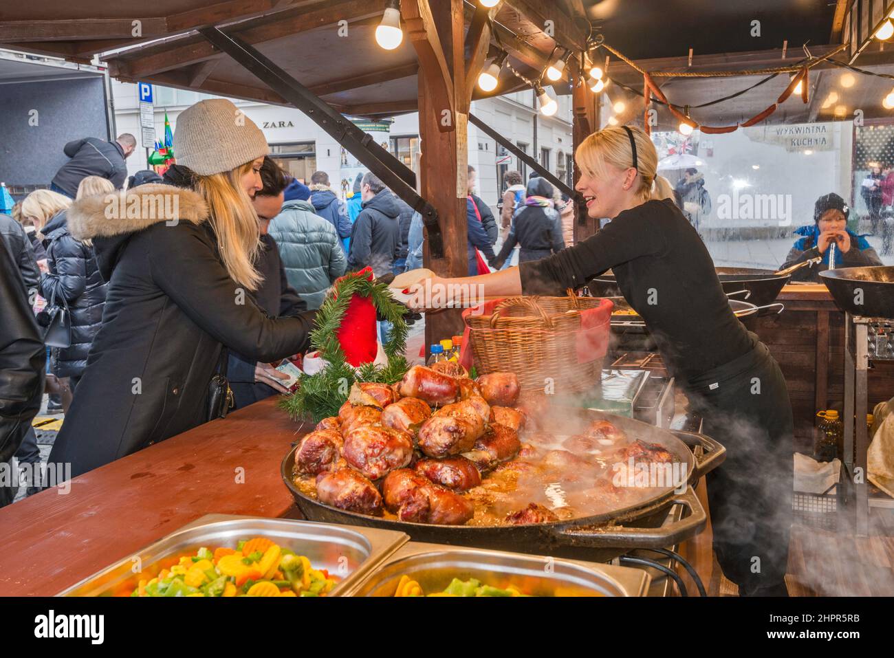 Customers, hot food at street stand at Christmas market, Main Market Square, Kraków, Poland Stock Photo