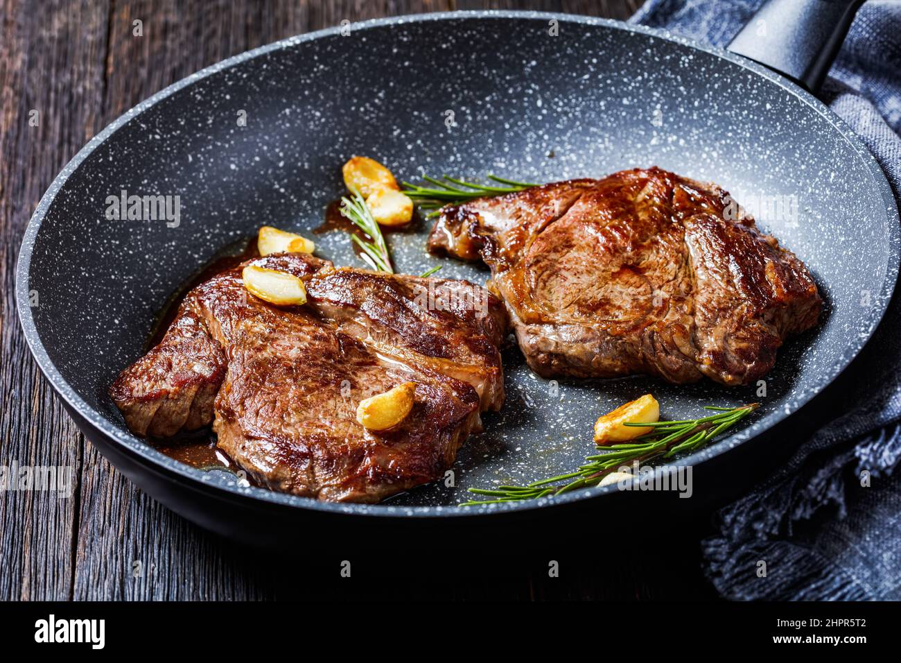 closeup of fried chuck eye beef steaks on a skillet with fried garlic