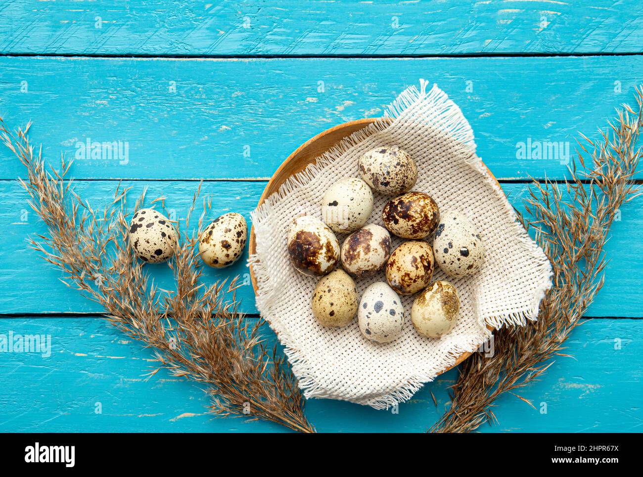 Pile of Quail eggs in natural color wood bowl indoors on blue wooden board background. Flat lay view, lot of copy space. Healthy food concept. Stock Photo