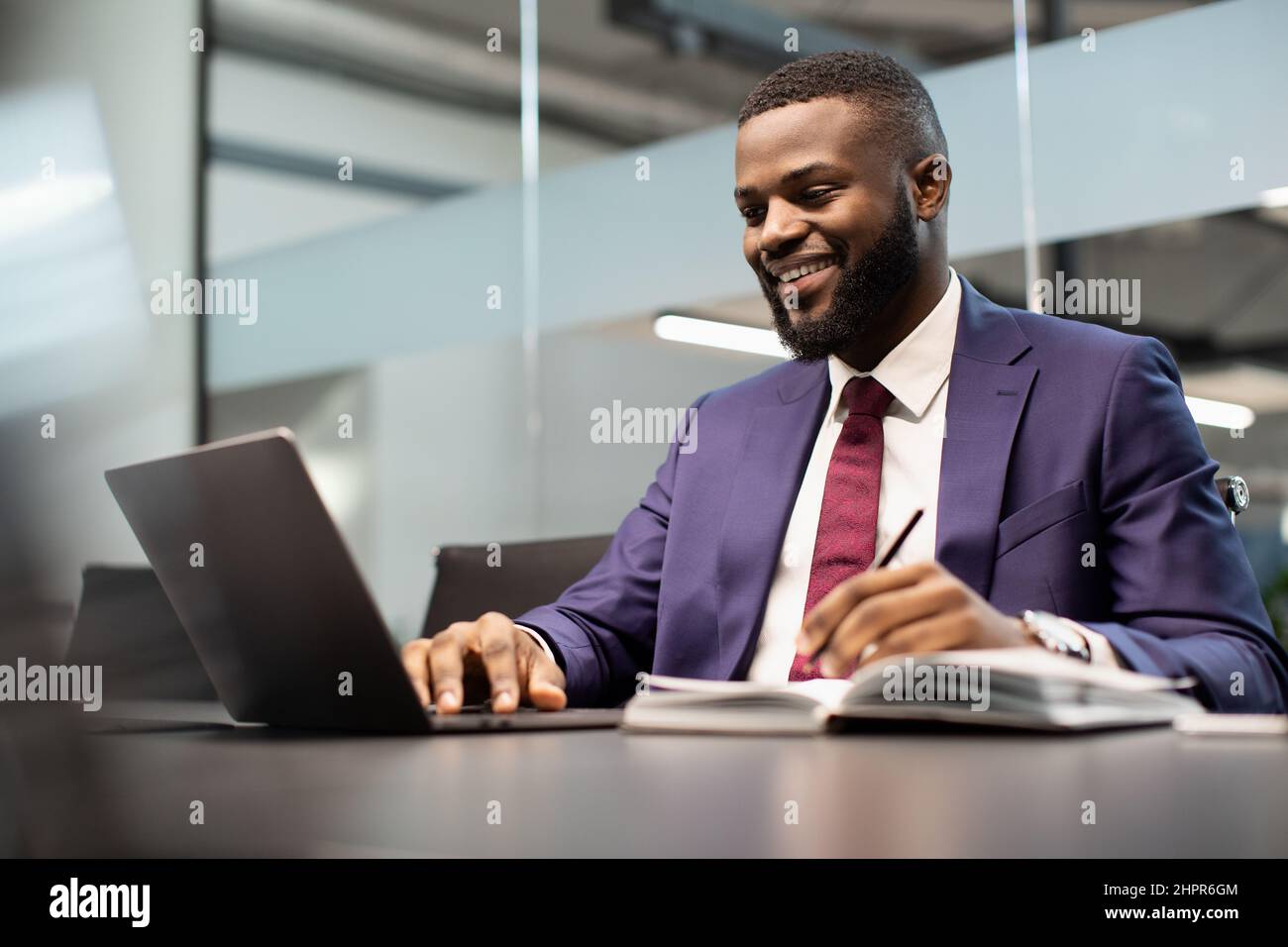 Smiling african american businessman using notebook and taking notes Stock Photo