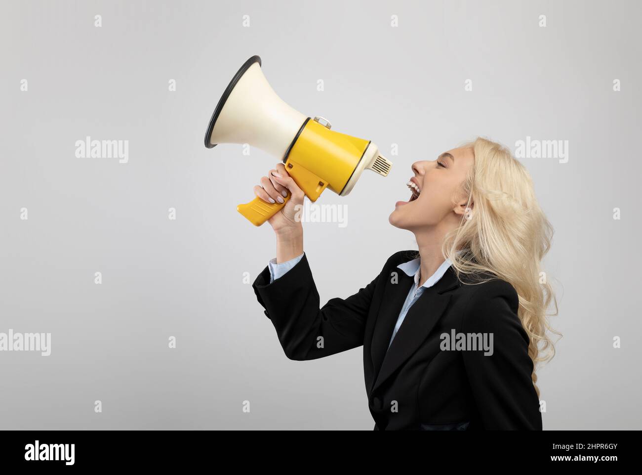Announcement concept. Businesswoman shouting with megaphone in hands, sharing news over light background Stock Photo