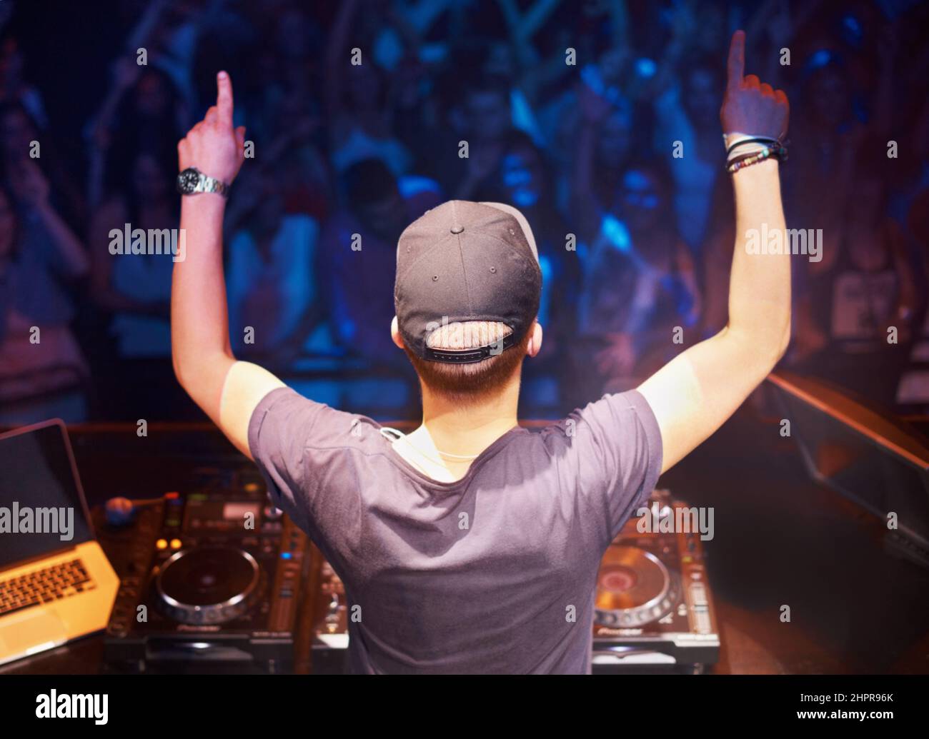 Spinning the wheels of steel. Rear view of a dj standing behind the decks with his hands in the air. Stock Photo
