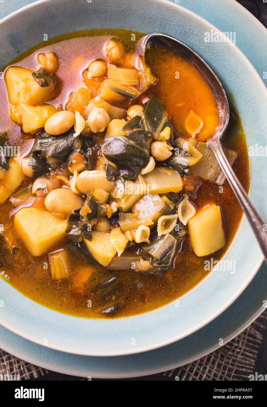 A blue bowl of Spanish chard stew with beans, potatoes, pork belly and