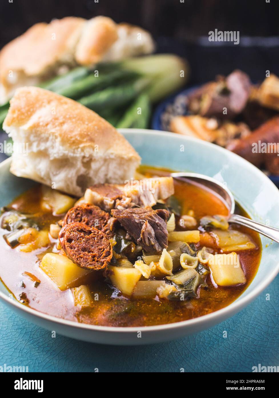 A blue bowl of Spanish chard stew with beans, potatoes, pork belly and