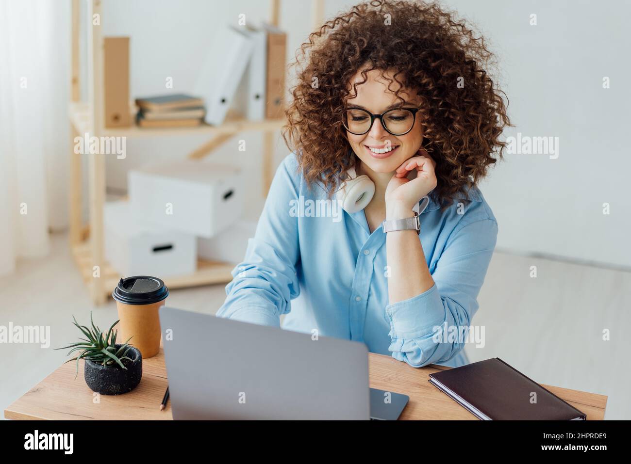 Young curly woman work on the notebook, drink coffee and talk on the phone. Work space. Office Stock Photo