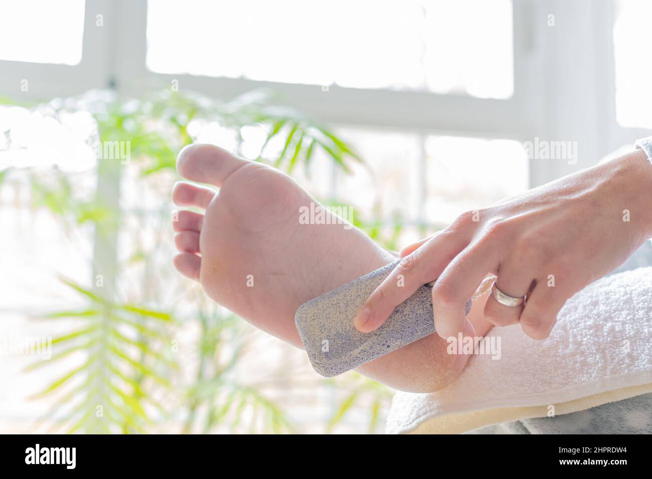 hands of a young woman using a pumice stone to soften calluses on her feet. concept body care