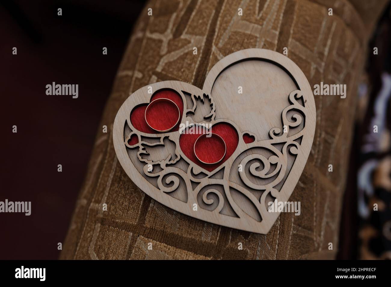 A pair of gold rings on a wooden stand in the shape of a heart Stock Photo
